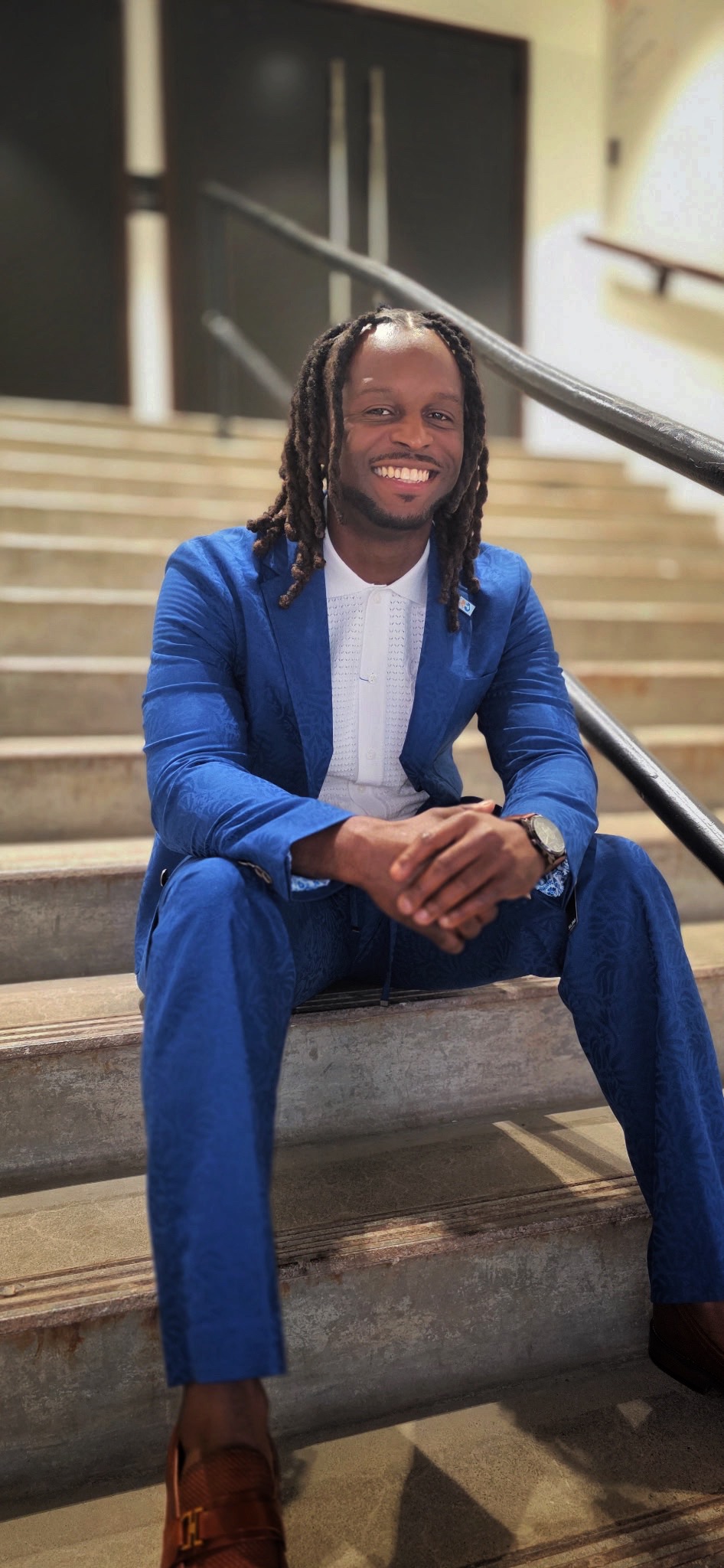Seth Irving smiling, seated on the steps in a blue suit